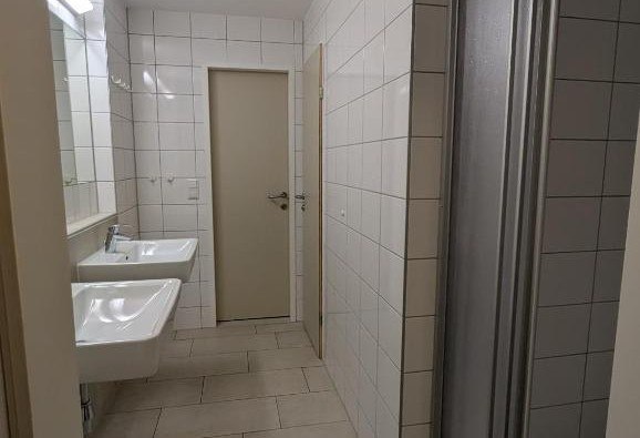 Ein Badezimmer mit zwei Waschbecken, weißen Fliesen und einer Tür.