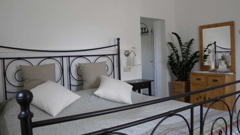 Bedroom with metal bed, chest of drawers and plant.