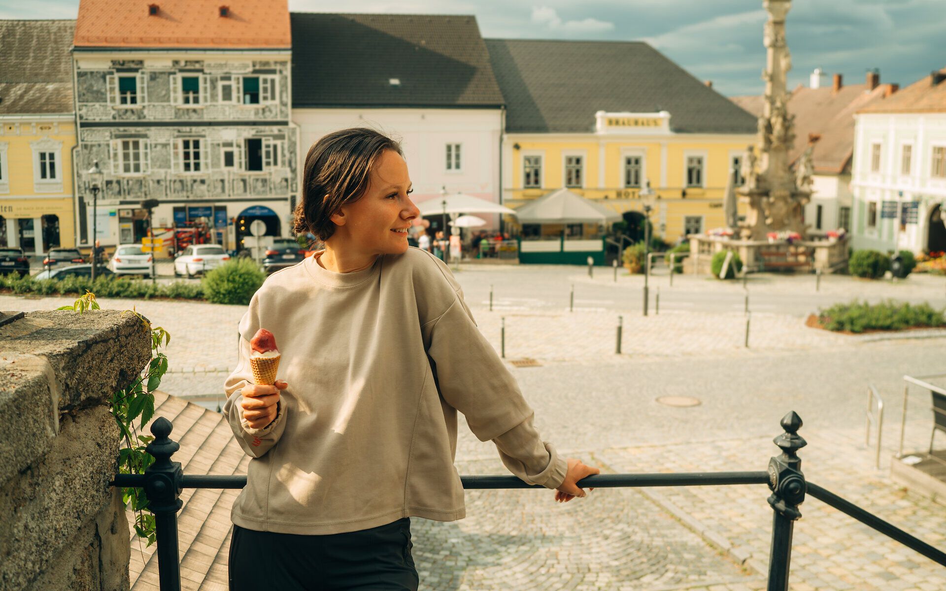 Eine Frau steht vor einem Geländer und blickt auf den Hauptplatz Weitra, mit einem Eis in der Hand.