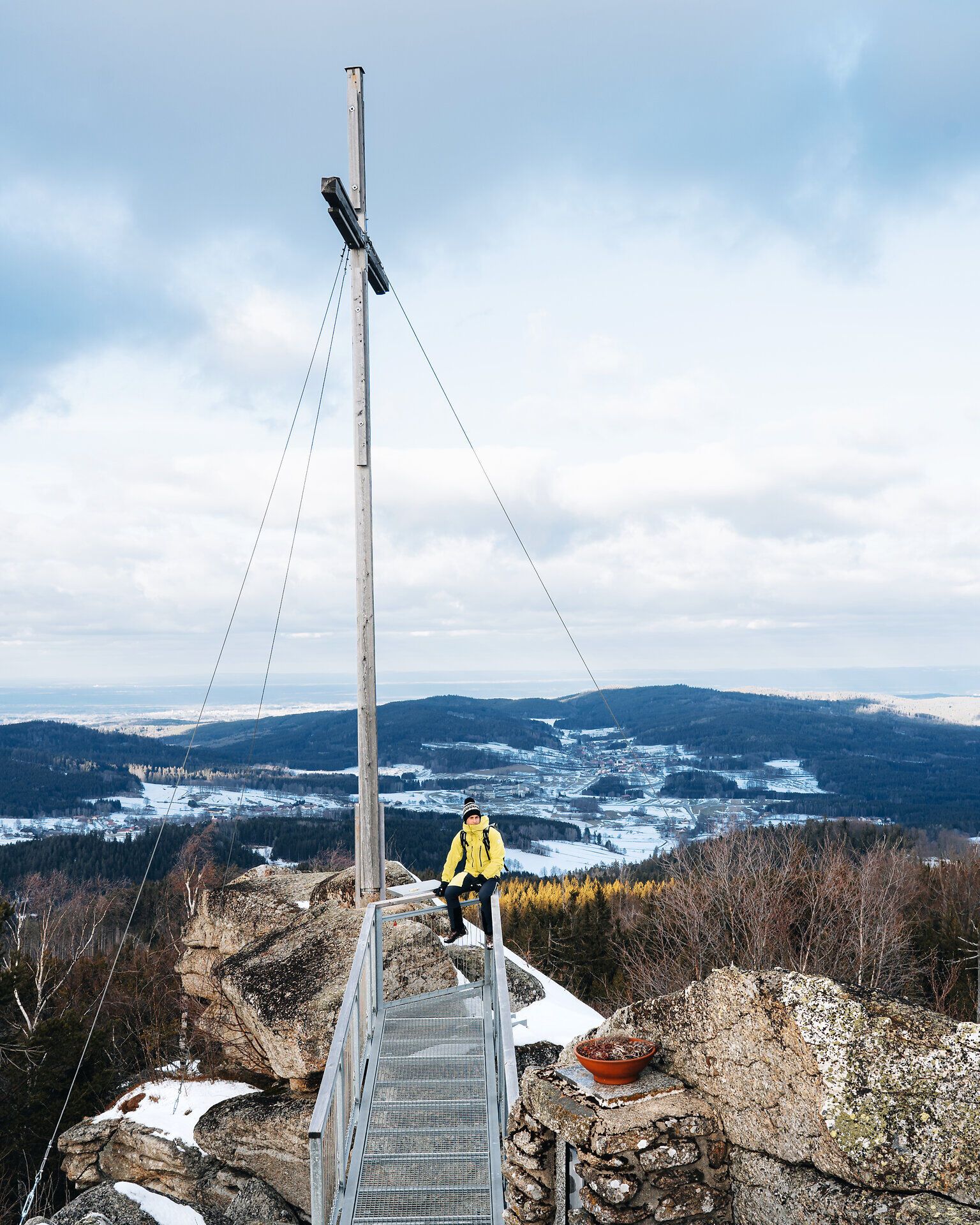 Ein strahlend gelber Wanderer genießt die frische Winterluft auf dem Nebelstein, während die schneebedeckten Berge in der Ferne eine majestätische Kulisse bieten. Der Blick über die verschneite Landschaft ist atemberaubend und lädt dazu ein, die Ruhe der Natur zu erleben.