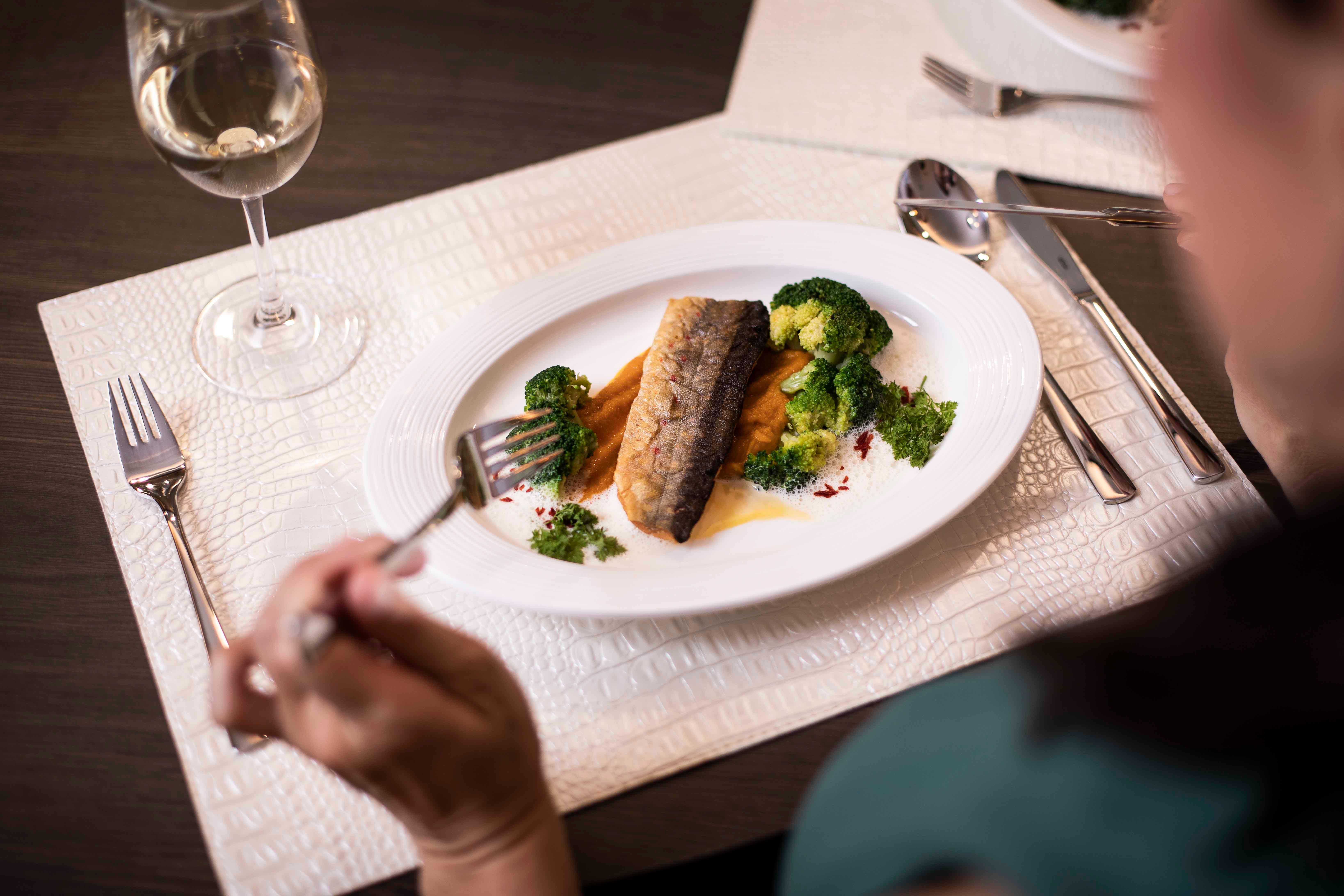 Ein Teller mit Fischfilet, Brokkoli und Soße, daneben ein Glas Weißwein.