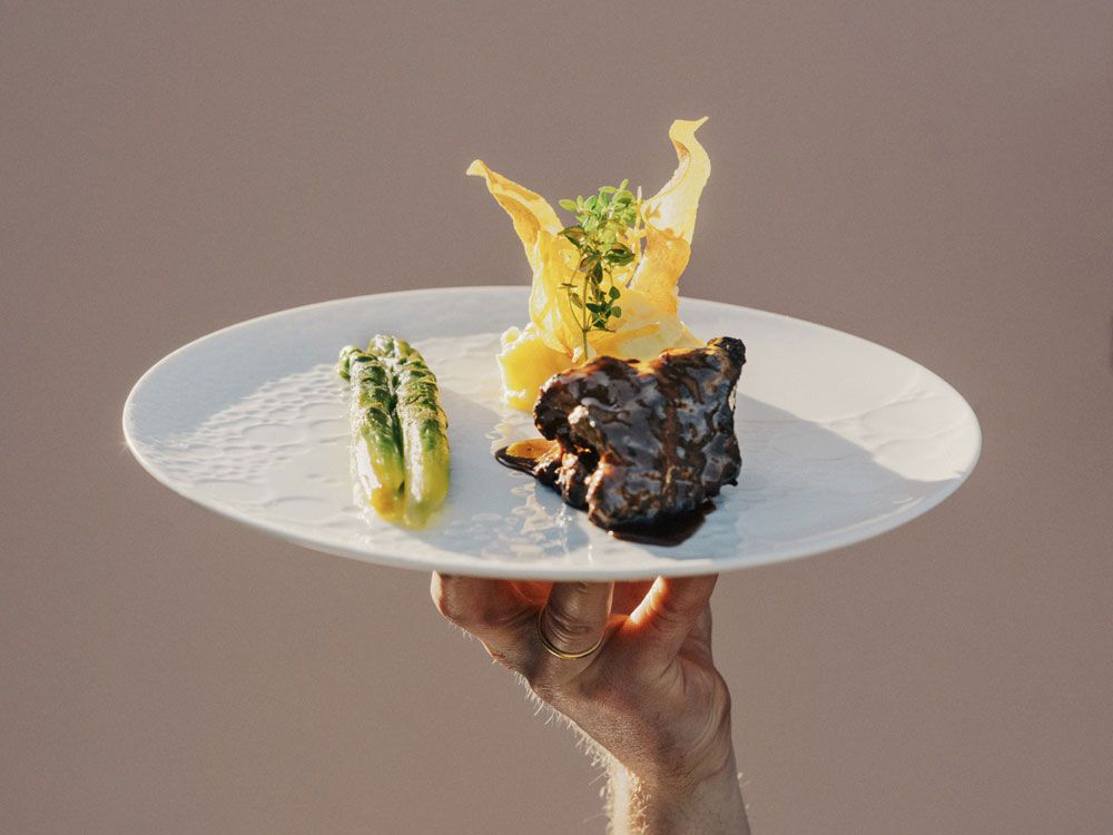 Ein Teller mit Angus Rind, Spargel und Kartoffelchips, von einer Hand gehalten.