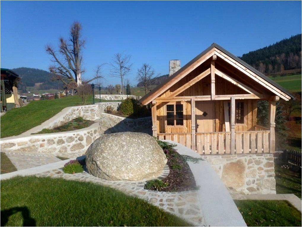 Kleines Holzhaus in einem Garten mit Steinmauern und großem Felsen.