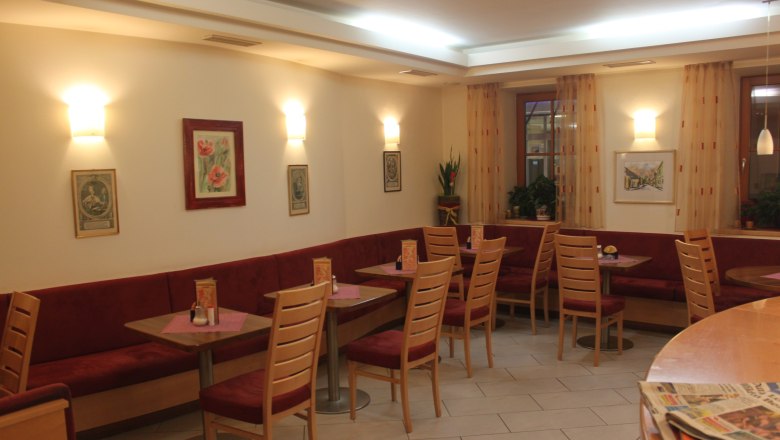 Innenansicht eines gemütlichen Cafés mit roten Sitzbänken und Holztischen.