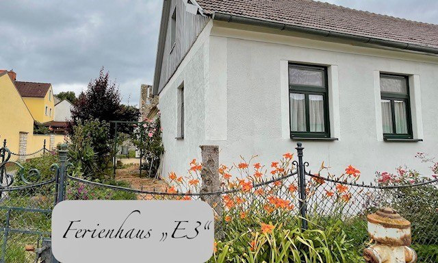 Außenansicht eines weißen Ferienhauses mit Garten und Blumen.