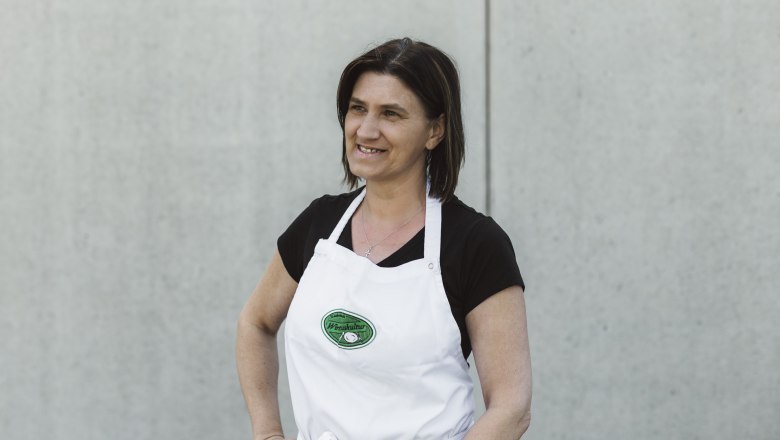 Frau in weißer Schürze vor grauer Wand.