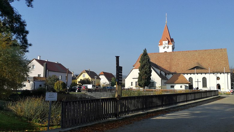 Pfarr- und Wallfahrtskirche Droß mit umliegenden Gebäuden und blauem Himmel.