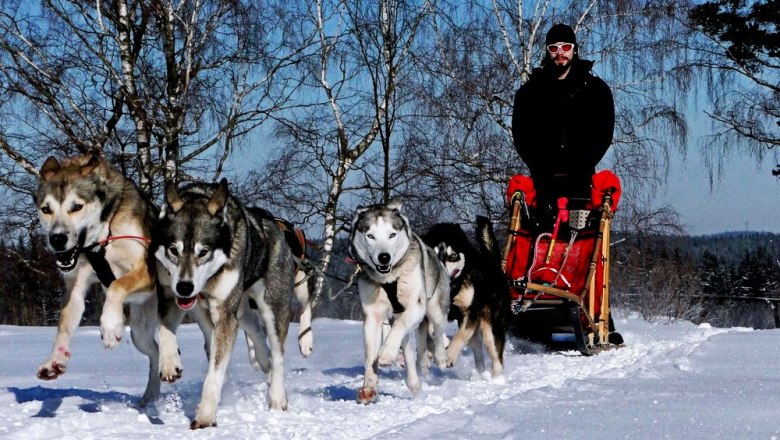 Ein Schlittenhundegespann zieht einen Schlitten durch eine verschneite Landschaft, gelenkt von einer Person in Winterkleidung.