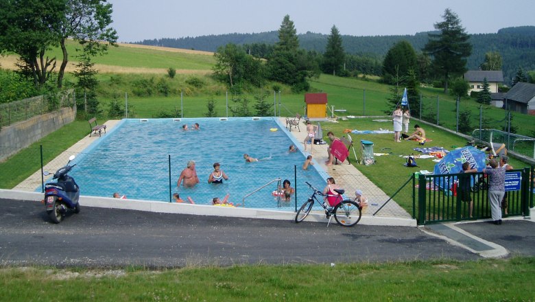 Ein Freibad mit mehreren Menschen, umgeben von grüner Landschaft und Bäumen.