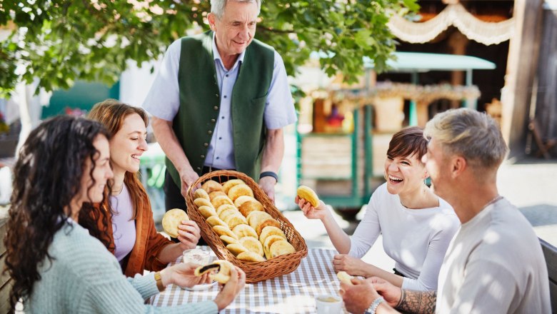 Der Mohnwirt serviert einer Gruppe von vier Personen Mohnzelten an einem Tisch im Freien.