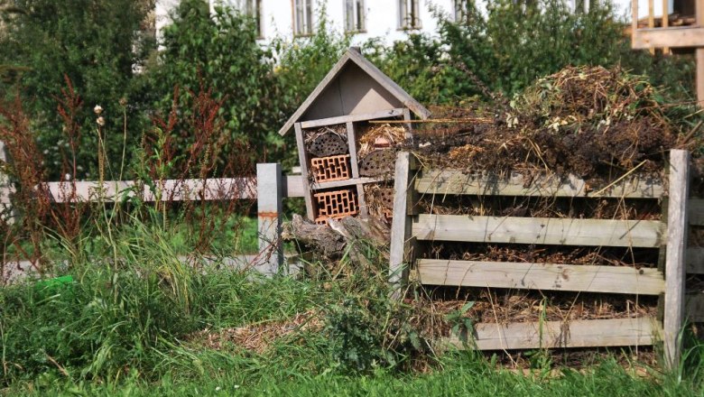Ein Insektenhotel neben einem Komposthaufen in einem Garten mit grünem Gras und Bäumen im Hintergrund.