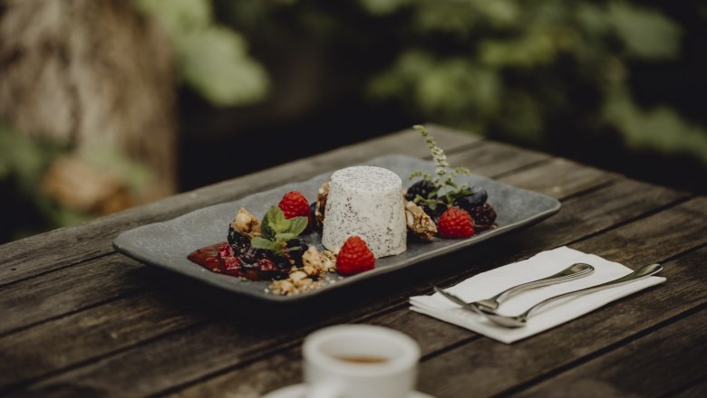 Poppy seed pannacotta with berries and nuts on a plate, served on an outdoor wooden table.