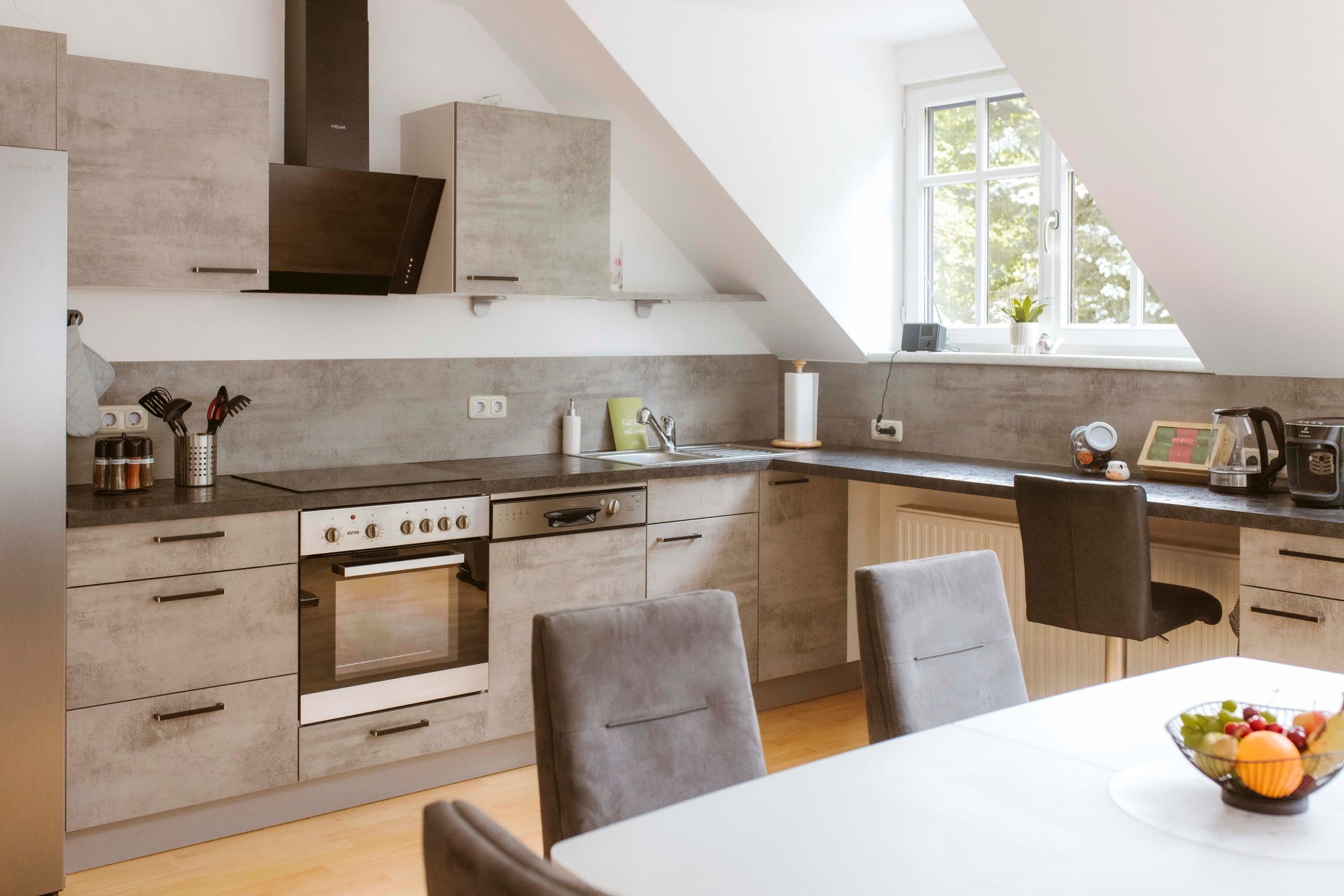 Moderne Küche mit grauen Schränken, Esstisch und Obstschale.