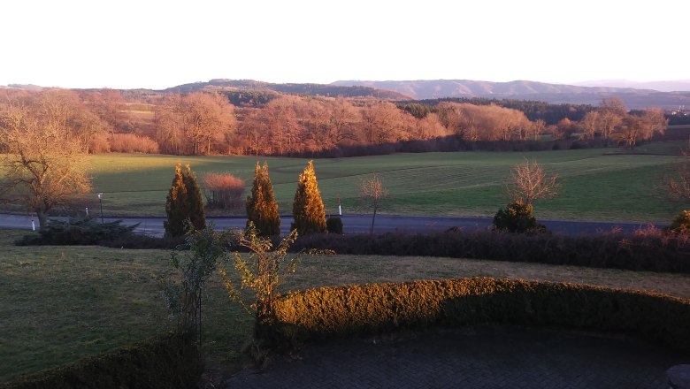 Landschaft mit Wiesen, Bäumen und Hügeln im Sonnenuntergang.