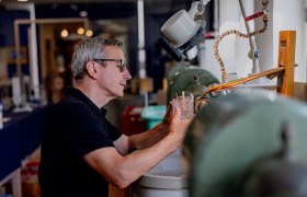 Ein Mann bearbeitet ein Glas an einer Schleifmaschine in einer Werkstatt.
