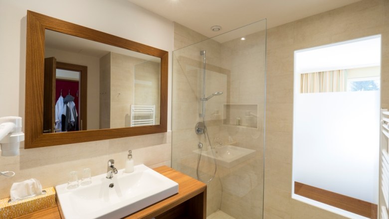 Modern bathroom with wooden details, washbasin, mirror and glass shower.