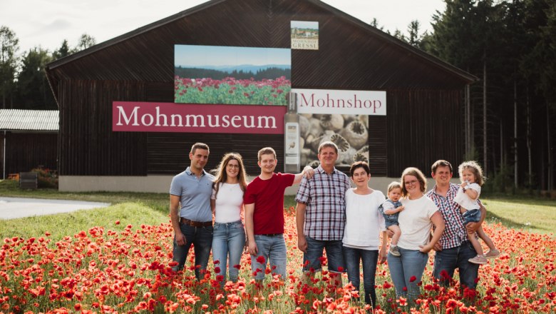 Eine Familie steht in einem Mohnfeld vor einem Gebäude mit der Aufschrift 'Mohnmuseum'.