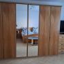 Schlafzimmer mit Holzschrank und Spiegel, Bett im Hintergrund.