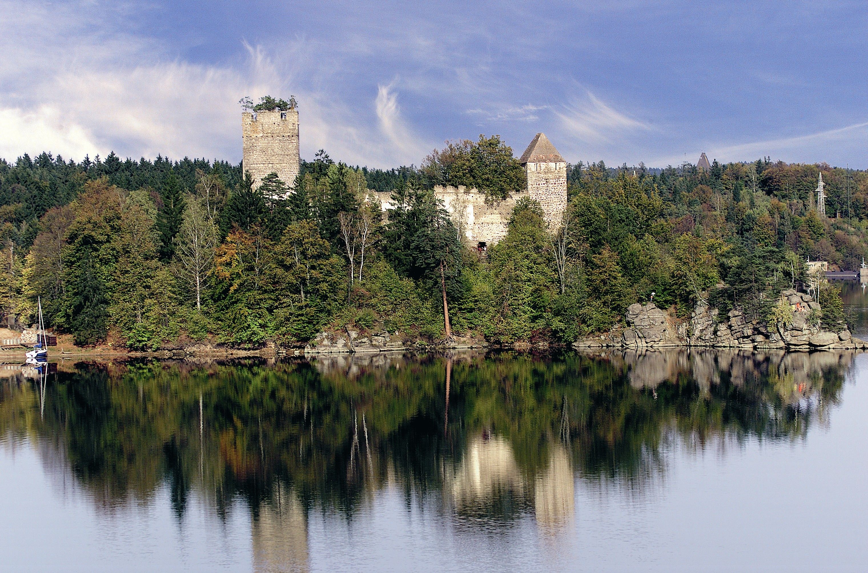 Ruine an einem Seeufer inmitten von Bäumen und Wald.