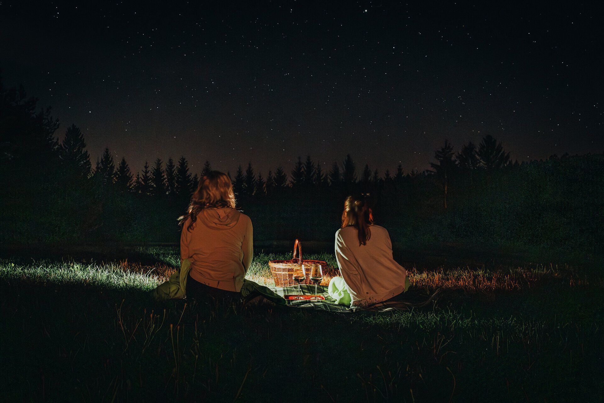 Unter dem funkelnden Sternenhimmel genießen zwei Freundinnen eine ruhige Nacht im Freien. Umgeben von der Stille der Natur und dem sanften Licht eines kleinen Picknicks, erleben sie einen unvergesslichen Moment der Verbundenheit und des Staunens.