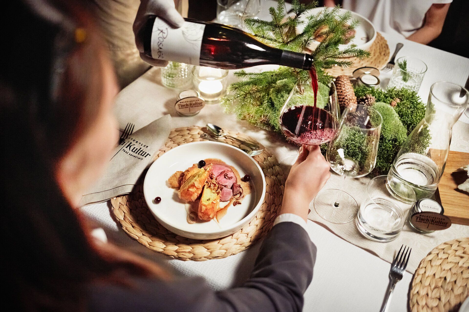 Ein festlich gedeckter Tisch lädt zu einem genussvollen Abendessen ein, während ein edler Rotwein in ein Glas fließt. Umgeben von der natürlichen Schönheit des Waldes, verspricht dieser Ort unvergessliche Momente der Geselligkeit und des Genusses.