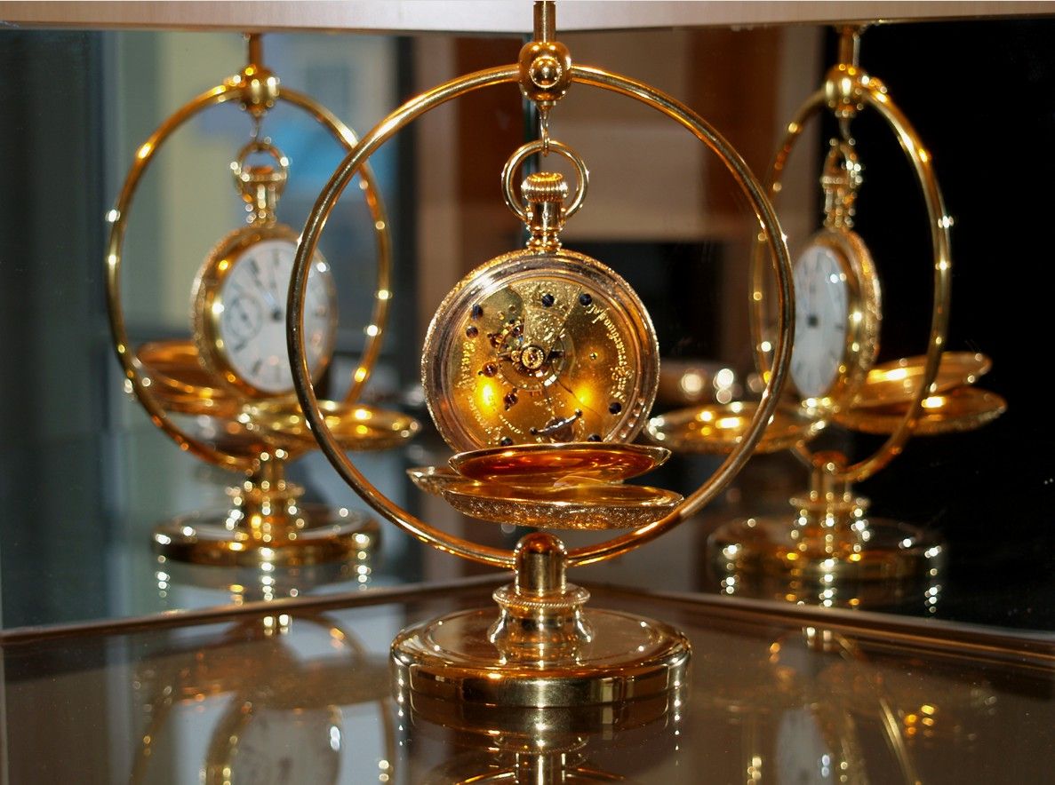 Goldene Taschenuhr in einem dekorativen Ständer, reflektiert in einem Spiegel.