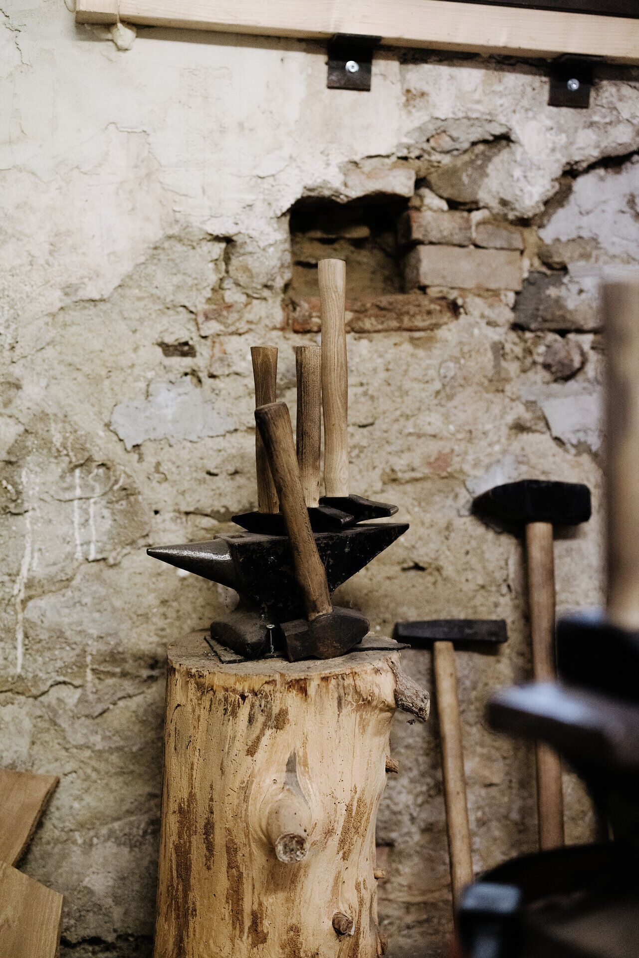 In einer rustikalen Werkstatt stehen handgefertigte Messer auf einem Baumstamm, umgeben von einer charmanten, alten Steinmauer. Die Atmosphäre ist geprägt von traditionellem Handwerk und der Liebe zum Detail, die in jedem einzelnen Stück steckt. Hier spürt man die Leidenschaft für das Schmieden und die Kunst des Messerbaus.