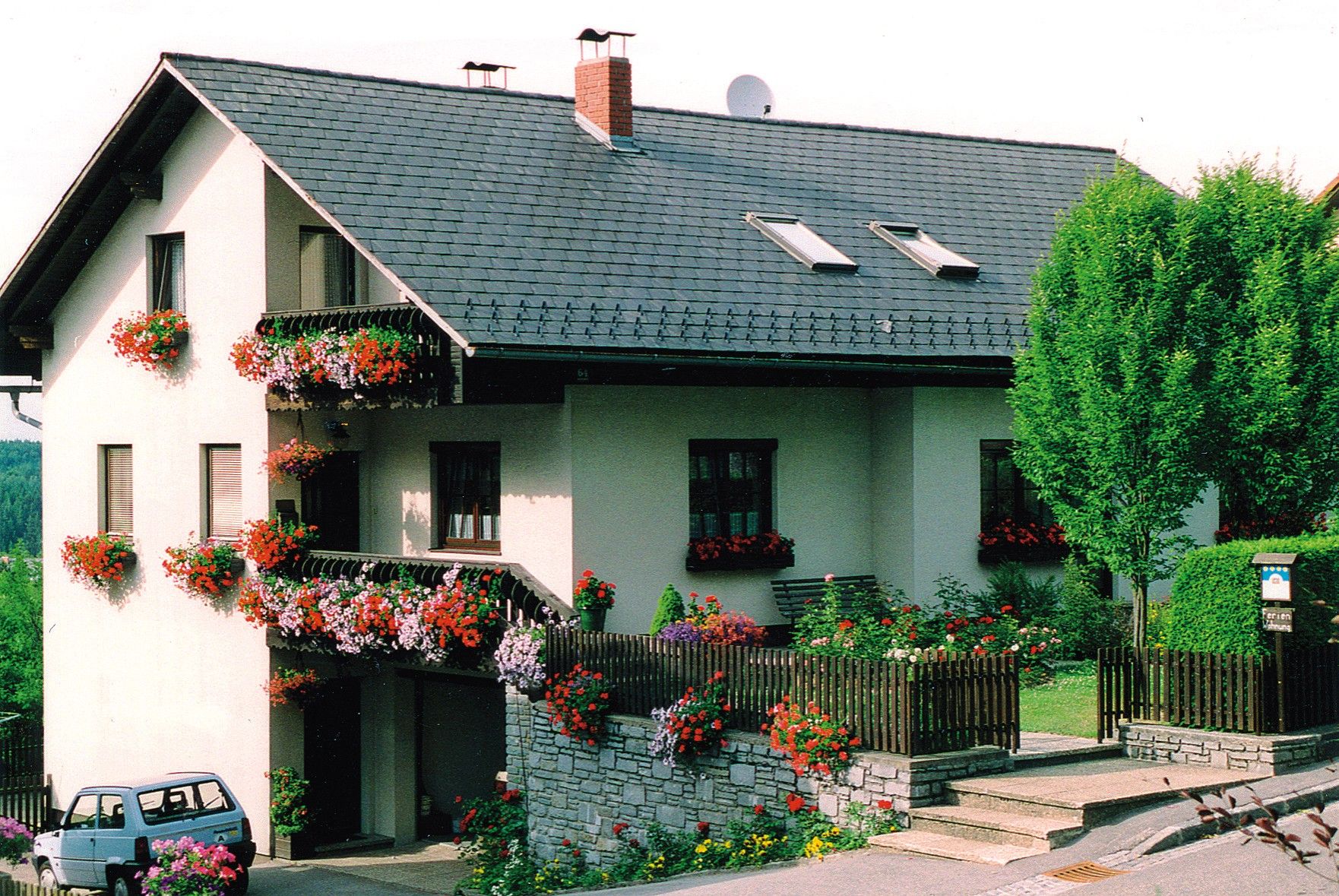 Ein zweistöckiges Haus mit Blumen geschmückten Balkonen und einem kleinen Garten.