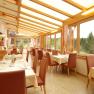 A bright conservatory of a restaurant with set tables and a view of a forest.