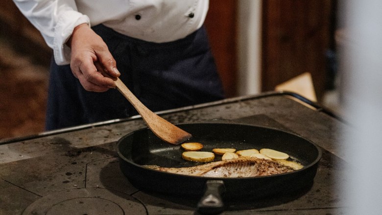 Ein Koch brät Fisch und Kartoffeln in einer Pfanne.