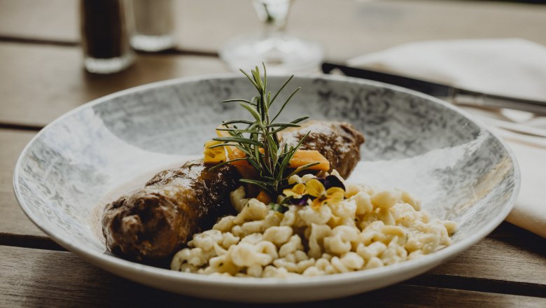 Ein Teller mit Rindsroulade, Spätzle und Gemüse, garniert mit Rosmarin und essbaren Blüten.