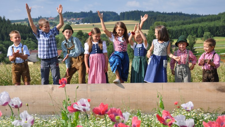 Kinder in traditioneller Kleidung stehen auf einem Feld mit Mohnblumen.