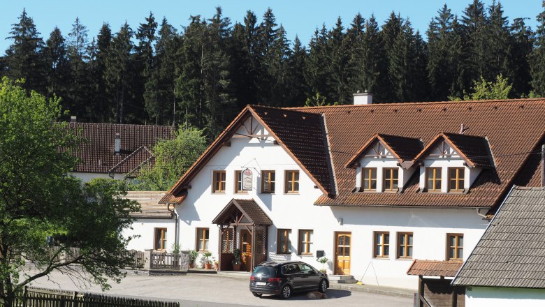 Ein traditionelles Gasthaus mit weißer Fassade und braunem Dach, umgeben von Bäumen und Wiese.