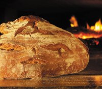 Ein frisch gebackenes Brot vor einem Holzofen mit Flammen.