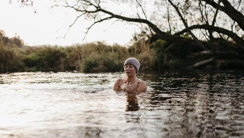 Person mit Mütze badet in einem Fluss bei kühlem Wetter.