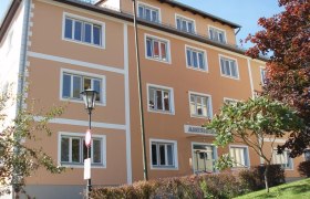 Ein dreistöckiges, orangefarbenes Gebäude mit weißen Fensterrahmen und einem Schild mit der Aufschrift 'Amtshaus'.