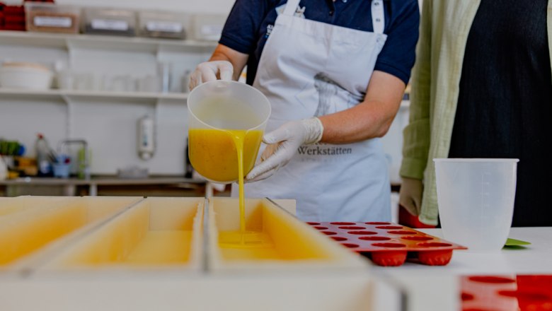 Person gießt gelbe Seife in rechteckige Formen in einer Werkstatt.