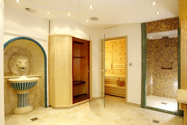 Innenansicht eines Wellnessbereichs mit Sauna, Dusche und Löwenkopfbrunnen.