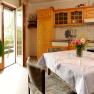 Gemütliche Küche mit Holzmöbeln, Esstisch und Blumenstrauß. Offene Balkontür mit Blick ins Grüne.