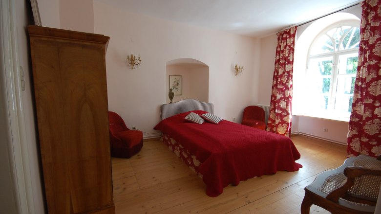 Ein gemütliches Schlafzimmer mit rotem Bett, roten Vorhängen und Holzmöbeln.