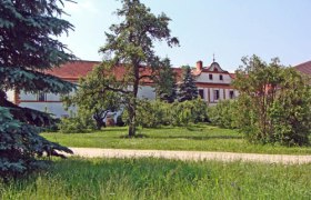 Ein historisches Gebäude mit rotem Dach, umgeben von Bäumen und grüner Wiese.
