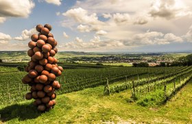 Skulptur aus Kugeln in Form einer Weintraube auf einem Weinberg mit Blick auf eine Landschaft.