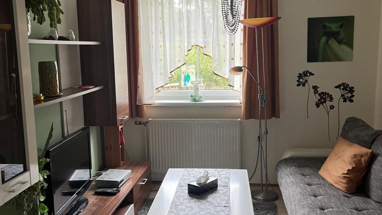 Gemütliches Wohnzimmer mit Sofa, Couchtisch, Teppich und Fernseher. Ein Kronleuchter hängt von der Decke, Pflanzen und Dekorationen sind sichtbar.