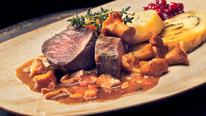Saddle of venison with chanterelle sauce and potato and herb roulade on a plate.