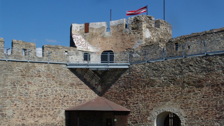 Alte Steinmauer mit österreichischer Flagge auf einem Turm.