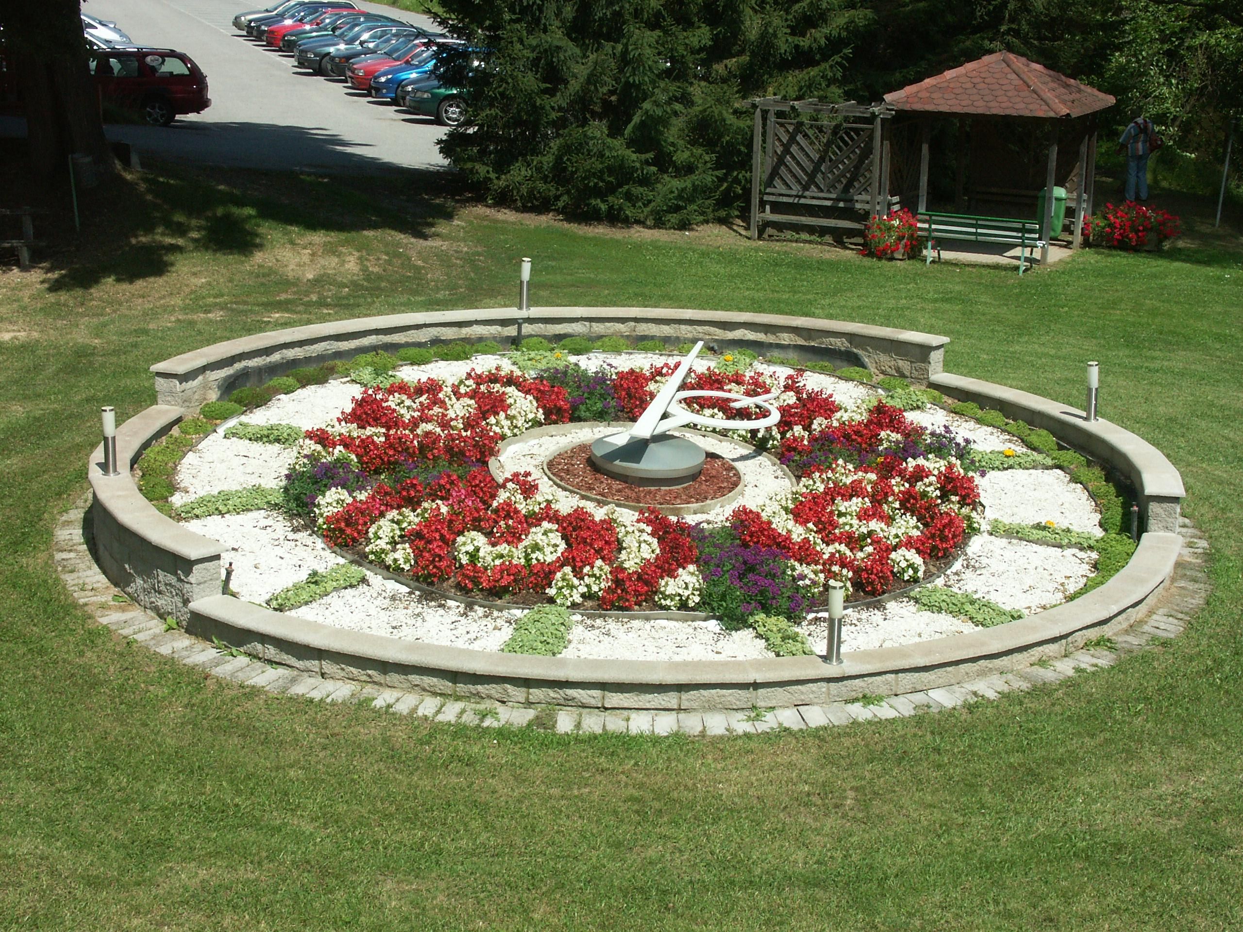 Blumenuhr in einem Park mit bunten Blumen und einem Pavillon im Hintergrund.