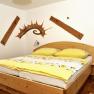 Ein gemütliches Schlafzimmer mit einem Doppelbett, gelber Bettwäsche und Holzmöbeln. An der Wand sind dekorative Holzelemente angebracht.