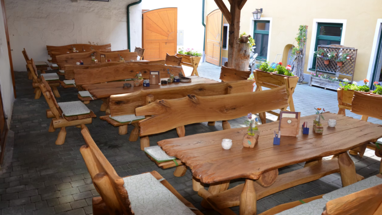 Rustikale Holzbänke und Tische in einem Gasthaus-Innenhof mit Blumen und Dekorationen.