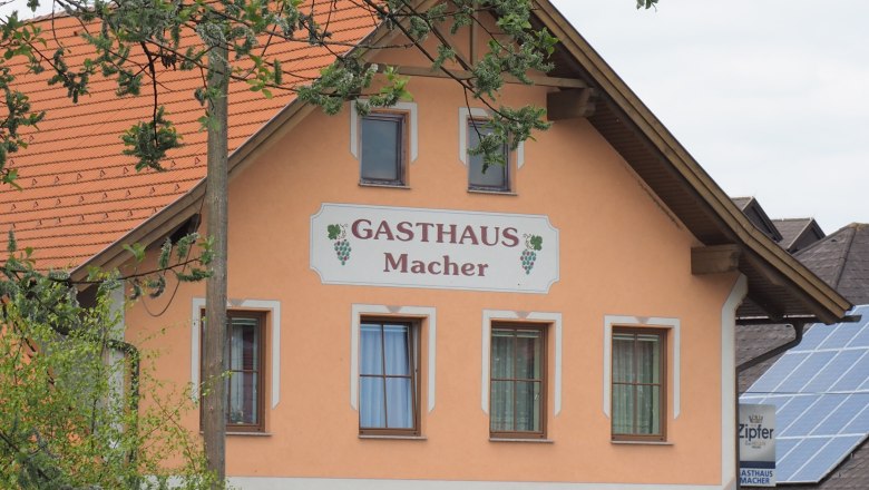 Ein traditionelles Gasthaus mit orangefarbener Fassade und roten Dachziegeln, umgeben von Bäumen.