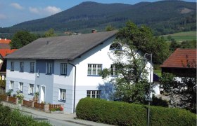 Ein großes, zweistöckiges, weiß-blaues Haus mit Garten und Berglandschaft im Hintergrund.
